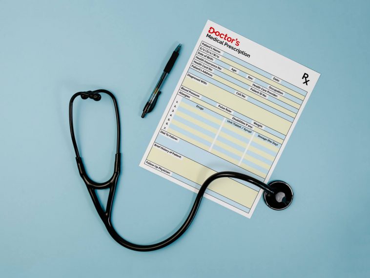 A mockup image of a doctor's prescription pad on a white background. The pad is open to a blank prescription with a stethoscope and medical tools placed on top of it.