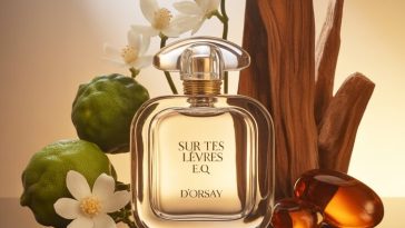 D’ORSAY Sur Tes Lèvres E.Q. perfume bottle on a reflective surface surrounded by bergamot, jasmine, sandalwood, and amber with soft golden lighting.